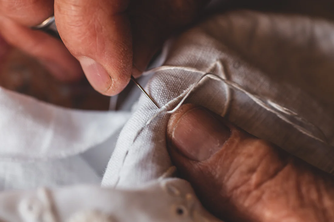 Hands sewing white fabric with needle and thread